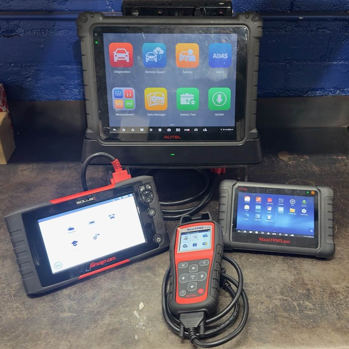 Four different handheld vehicle scanning tools, placed next to each other on a workbench.